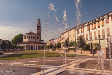 Rovigo, İtalya 21 Haziran 2025, Roma 'daki Piazza Matotti kaldırımından yükselen su jetleri ve arka planda kilise ve çan kulesi.