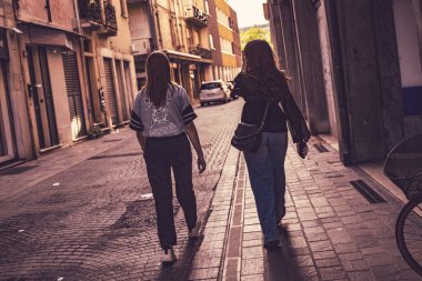 Rovigo, İtalya, 21 Haziran 2025. İki kadın turist, İtalya 'nın Rovigo şehrinde dar bir sokakta yürüyüp yaz öğleden sonranın tadını çıkarıyorlar.