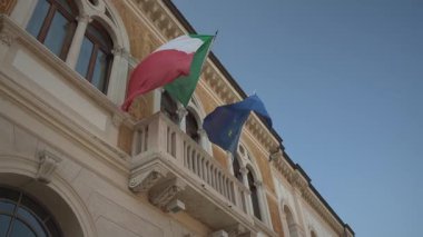 Rovigo, İtalya 21 Haziran 2025, İtalya ve Avrupa Birliği bayrakları rüzgarda hafifçe sallanıyor, İtalya, Rovigo 'da bir binanın balkonuna bağlı.