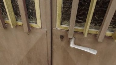 Milan, İtalya 21 Haziran 2025, adam eski, kahverengi, cam paneller ve metal detaylarla dolu ahşap bir kapıyı açıyor.