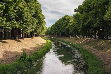 Naviglio martesana kanalı İtalya 'nın Gorgonzola kasabasında yavaşça akar, yemyeşil ağaçlarla kaplanır ve yaz gökyüzünü yansıtır.