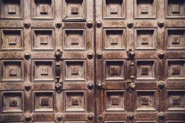 Karmaşık oymalar ve metal çivilerin yer aldığı eski bir ahşap kapıyı kapatın. Geçmiş dönemin işçiliğini ve kaliteli malzemelerin kalıcı doğasını vurgulayın.