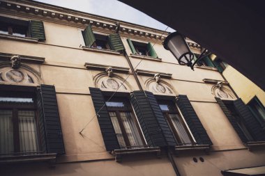 Padova, İtalya 30 Haziran 2025, yeşil kepenkleri, dekoratif kafaları ve İtalya 'nın Padova şehrinde bir sokak lambası olan bir binanın düşük açılı görüntüsü.