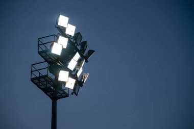 Güçlü stadyum ışıkları alacakaranlık gökyüzüne karşı parlayarak heyecan verici bir beklenti atmosferi yaratıyor.