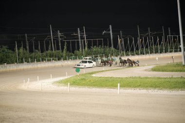 Padua, İtalya 8 Temmuz 2025. Atlar ve sürücüler parlak ışıklar altında heyecan verici bir koşum takımı yarışında yarış halindeler.
