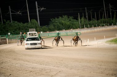 Padua, İtalya 8 Temmuz 2025, gece koşum takımı atlarla yarışıyor ve toprak yolda volta atan bir araba, yemyeşil ve elektrik hatlarıyla çevrili.