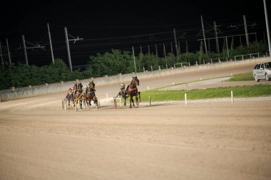 Padua, İtalya 8 Temmuz 2025. Atlar ve jokeyler yoğun bir koşum takımı yarışına girdiler. İyi aydınlatılmış bir pistte.