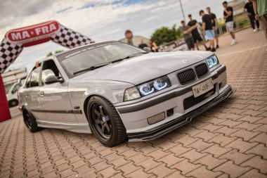 Roma, İtalya 18 Temmuz 2025, gri ayarlı BMW E36 yavaşça şişme kemerin altından geçiyor bir araba toplantısında, arka planda izleyenler