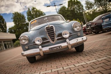 Roma, İtalya 18 Temmuz 2025, açık mavi bir alfa romeo önü 1900 tuğla zeminde park edilmiş diğer araba ve ağaçların arka planında.