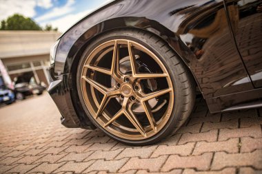 Roma, İtalya 18 Temmuz 2025, siyah bir spor arabadaki bronz alaşımlı tekerleğin alçak açılı görüntüsü, tuğla kaldırıma park edilmiş.