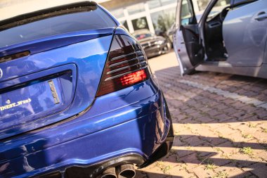 Roma, İtalya 18 Temmuz 2025, mavi ayarlı spor bir arabanın dikiz görüntüsü güneş ışığının altındaki tuğlalı bir otoparka park edilmiş.