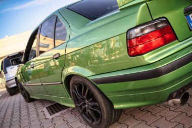 Roma, İtalya 18 Temmuz 2025. Otoparka park edilmiş yeşil BMW. Tanımlanamayan insanları yansıtan kaldırım taşlarından yapılmış.