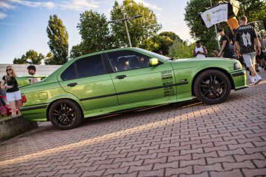 Roma, İtalya 18 Temmuz 2025, arka planda insanlarla buluşurken yeşil BMW aracını tuğla kaldırıma park etmiş.