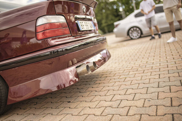 Rome, italy 18 july 2025, tuned red bmw e36 sedan showcasing aftermarket exhaust system, parked on a brick paved surface