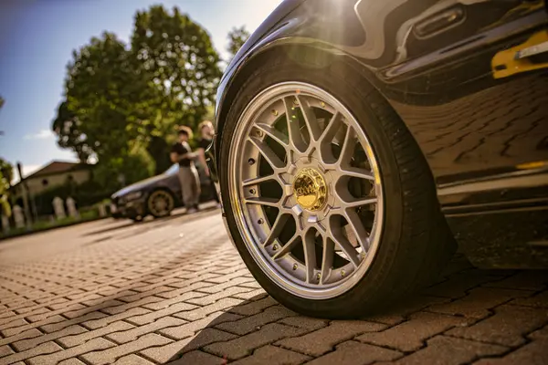 Roma, İtalya 18 Temmuz 2025, park halindeki bir spor arabanın parlak alaşımlı tekerine yakın çekim, tuğla kaldırımı ve güneş ışığını yansıtıyor.