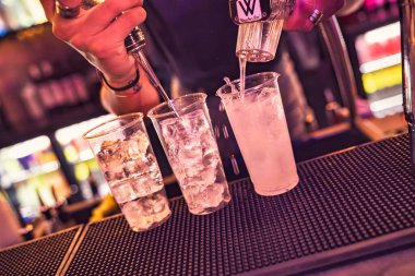 Barmen plastik bardaklarda buzla kokteyl hazırlıyor. Gece kulübünde metal bir sprey kullanıyor.