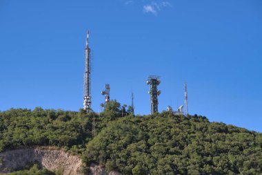 Birçok telekomünikasyon kulesi açık mavi gökyüzüne karşı yemyeşil bir tepenin üzerinde duruyor. Bu da İtalya 'nın kırsal kesimlerinde bağlantıyı sağlıyor.
