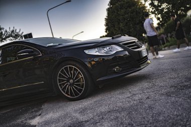 Calaone, İtalya 13 Ağustos 2025: şık siyah Volkswagen cc gün batımında asfalt yola park edilmiş.