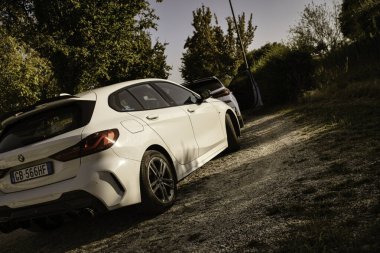 Calaone, İtalya, 13 Ağustos 2025: çakıllı bir yola park edilmiş şık beyaz bmw, bereketli yeşillik ve ağaçlarla çevrili doğanın huzurunun tadını çıkarıyor.