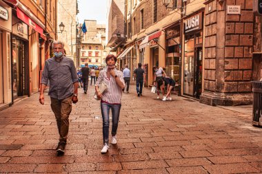 Bolonya, İtalya 19 Ağustos 2025: Bologna, İtalya 'da şehir merkezinde tipik bir alışveriş caddesinde yürüyen ve ameliyat maskesi takan bir çift.