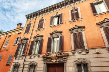 Modena, İtalya 20 Ağustos 2025: Kahverengi panjurlu ve dekoratif mimari detayların yer aldığı tarihi bir binanın turuncu cephesi, Modena, İtalya