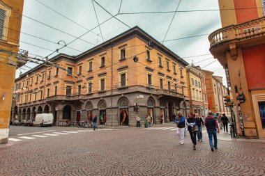 Modena, İtalya 20 Ağustos 2025: Modena, İtalya 'da tarihi binalar ve tramvay kabloları manzaralı bir kaldırım taşı caddesinde yürüyen insanlar