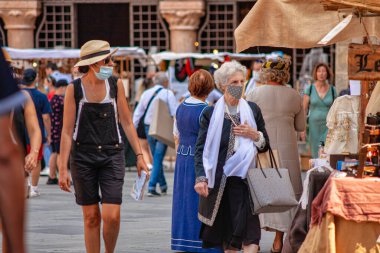 Verona, İtalya 20 Ağustos 2025: Maskeli insanlar Verona, İtalya 'da kalabalık bir açık hava pazarında tezgah ve dükkanların arasında yürüyorlar.