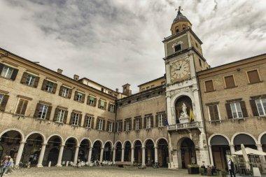 Modena, İtalya 20 Ağustos 2025 Piazza Grande 'deki tarihi bina saat kulesi, kemerler ve bulutlu gökyüzü.