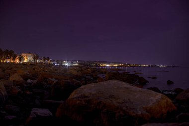 Civitavecchia, İtalya, 20 Ağustos 2025: Kayalık kıyılardan alacakaranlıkta Tyrhenian denizi üzerinde sıcak bir parıltı bırakarak, İtalya 'nın Sivitavecchia kentsel manzarası aydınlandı