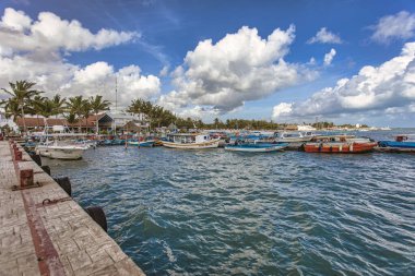Isla Mujeres, Meksika. 20 Ağustos 2025. Güneşli bir günde mavi gökyüzü ve tüylü beyaz bulutlarla dolu renkli tekneler Isla Mujeres, Meksika 'ya yanaşıyor.