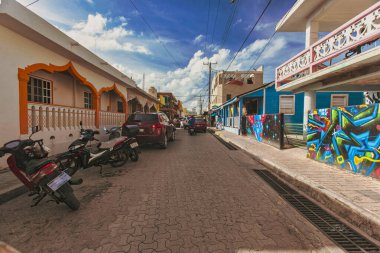 Isla Mujeres, Meksika 20 Ağustos 2025 Isla Mujeres, Meksika 'da canlı bir sokak sahnesi renkli binalar, sokak sanatı ve güneşli mavi gökyüzü altında park edilmiş araçlar.
