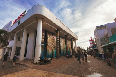 Isla Mujeres, Meksika 20 Ağustos 2025: Meksika 'da Isla Mujeres, Meksika' da Hidalgo Bulvarı 'nda bir duvar resminin yanında yürüyen turistler ve arka planda bir deniz feneri var.