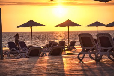 Sahil sandalyeleri ve renkli şemsiyeler Dominik Cumhuriyeti kıyı şeridinde güneş okyanusun üzerinde batarken sakin bir atmosfer yaratıyor.