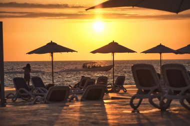 Dominik Cumhuriyeti 'nde güneş şemsiyeleri ve şezlonglarla gün batımını seyreden turistler, bir tekne geçerken...