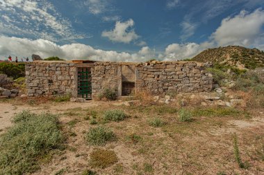 Kırılan taş yapı, yeşil metal bir kapı ile mavi gökyüzüne karşı duruyor. Yumuşak beyaz bulutlar punta molentis, sardunya, İtalya