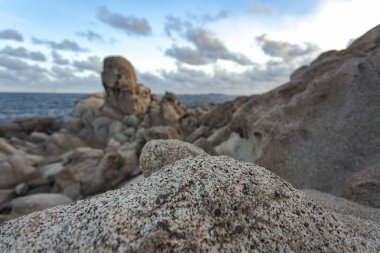 Punta Molentis plajında granit kaya oluşumlarının yakın plan çekimi, turkuaz Akdeniz ve arka planda bulutlu gökyüzü
