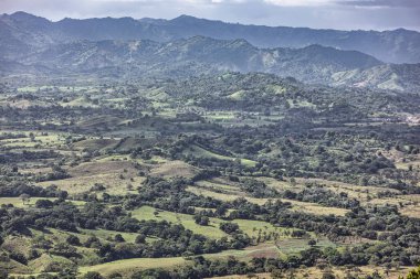 Yuvarlanan yeşil tepeler ve vadiler Dominik Cumhuriyeti 'nin manzaralı montaa redonda' sında bulutlu bir gökyüzünün altında güneş ışığıyla yıkanır..