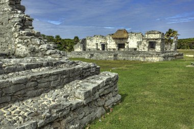 Antik Maya harabeleri Tulum, Meksika 'da görkemli bir şekilde duruyor. Karmaşık taş işleri ve parlak mavi gökyüzüne karşı sazdan bir çatı sergiliyorlar.