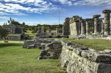 Tulum arkeoloji sahasındaki antik Maya kalıntılarının manzaralı manzarasında, verimli yeşillik ve Karayip denizlerinin zeminine karşı iyi korunmuş yapılar sergileniyor.