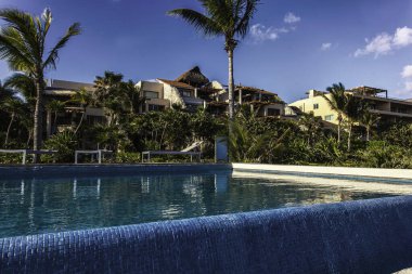 Mavi fayanslı sakin sonsuzluk havuzu Puerto aventuras, Riviera Maya 'daki yemyeşil tropikal bitki örtüsünün ortasındaki lüks bir tatil köyünün çarpıcı manzarasını sunuyor.