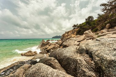 Turkuaz dalgalar Monte Turnu, İtalya 'da bulutlu bir gökyüzünün altında kayalık bir kıyı şeridine çarpıp dramatik ve pitoresk bir manzara yaratıyor.