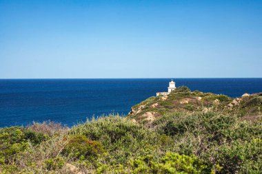 Koyu mavi Akdeniz manzaralı bir tepede duran beyaz deniz fenerinin manzarası Capo Ferrato, Sardunya ve İtalya 'nın engebeli güzelliğini vurguluyor.