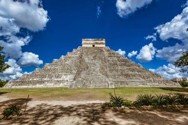 Meksika, Yucatan 'daki Chichen itza arkeolojik alanının ana piramidi El Castillo, tüylü beyaz bulutlarla kaplı canlı mavi gökyüzüne karşı dimdik ayakta duruyor.