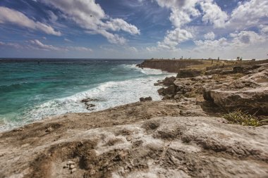Isla Mujeres 'in kayalık kayalıklarına çarpan turkuaz dalgaların nefes kesici görüntüsü. Canlı mavi gökyüzünün altında bir helikopter yükseliyor.