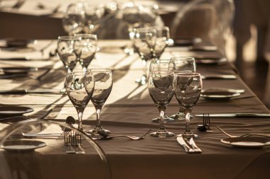 Boş şarap kadehleri ve çatal bıçak takımı bir restoranda uzun bir masanın üzerine konur ve günbatımında yapılacak bir etkinlik için zarif bir ortam yaratır.