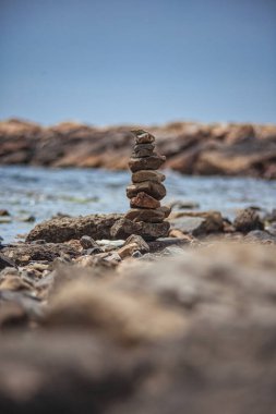 Kayalık bir sahilde duran taş kule dengeyi, farkındalığı ve huzuru temsil ediyor.