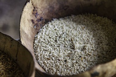 Ahşap bir kaseyi dolduran cilalanmış pirinç taneleri, işlenmemiş kahverengi pirinçle bir kasenin yanına yerleştiriliyor, işlem ve görünüşteki farklılıkları vurguluyor.