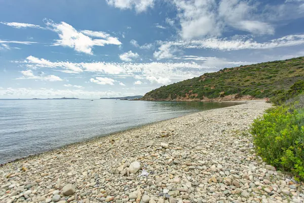 Sakin sular Punta Molentis sahilinin çakıl taşlarını yavaşça yıkıyor. Kötüler, sardunya, İtalya, bulutlarla kaplı parlak mavi bir gökyüzünün altında.