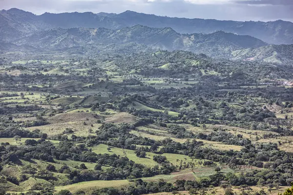 Yuvarlanan yeşil tepeler ve vadiler Dominik Cumhuriyeti 'nin manzaralı montaa redonda' sında bulutlu bir gökyüzünün altında güneş ışığıyla yıkanır..