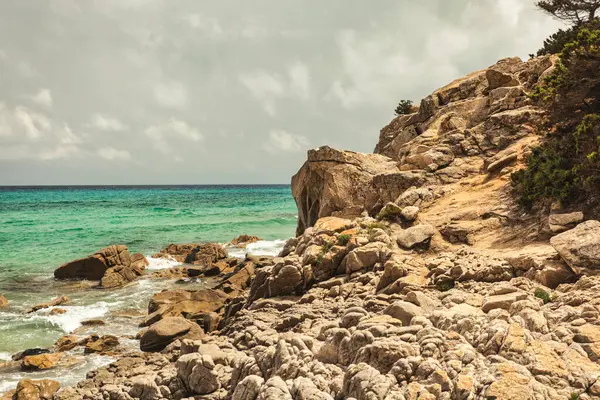Monte Turnu, İtalya 'nın kayalık kıyı şeridinde nefes kesici bir manzara gözler önüne seriliyor. Turkuaz sular dramatik bulutlu bir gökyüzü altında engebeli kayalarla buluşuyor.